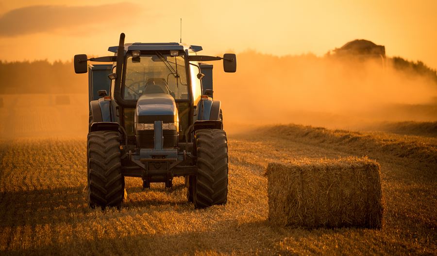 tractor driving in field next to hay bale